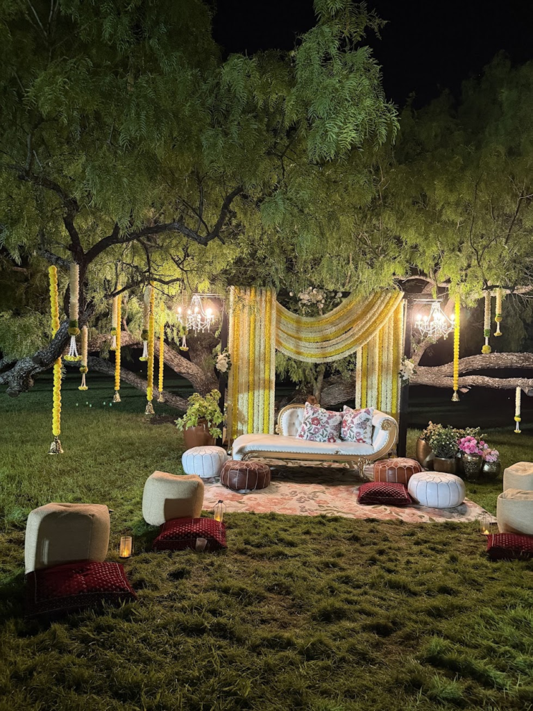 Floral garlands, chandeliers and lounge seating beneath the trees at night
